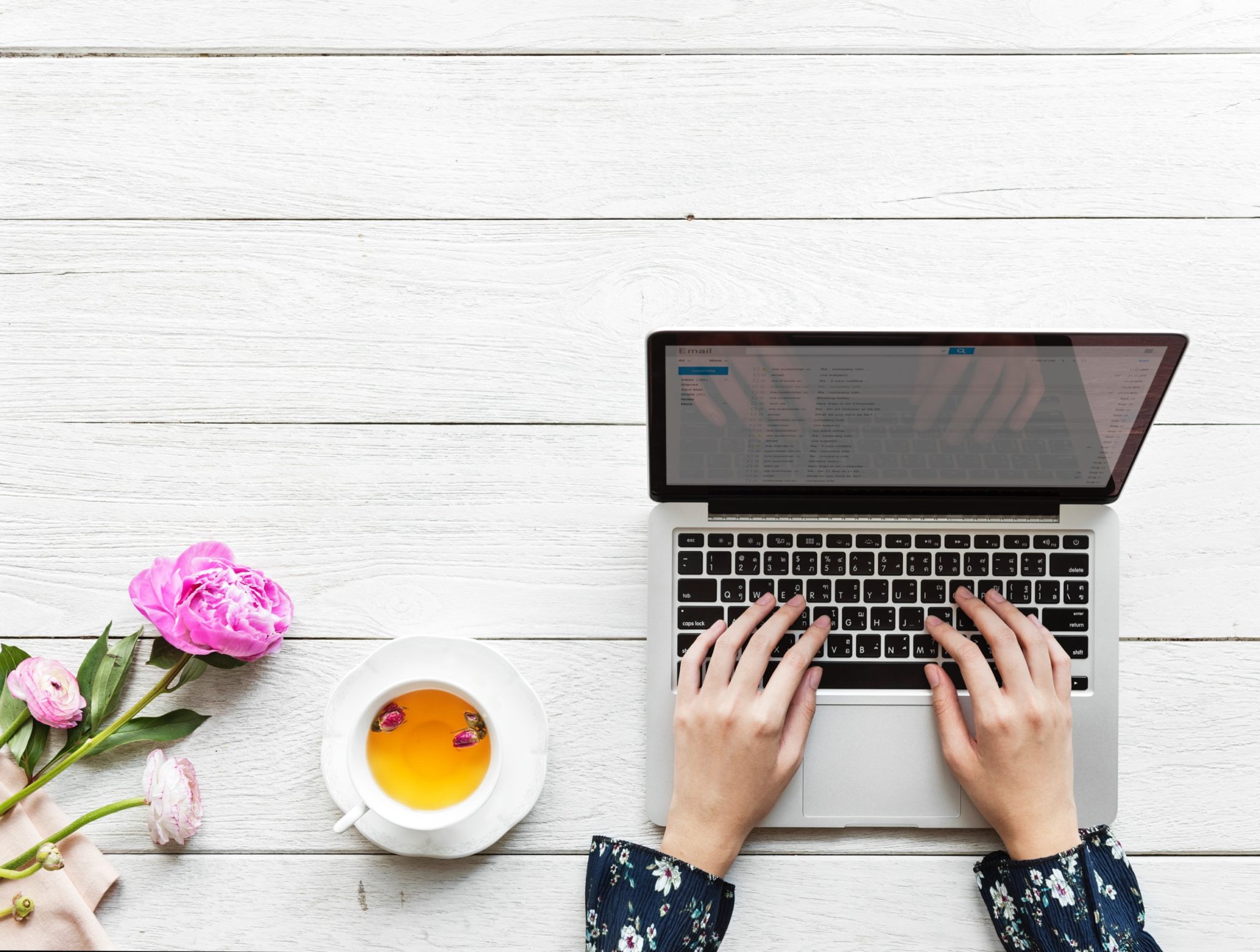 woman using an apple laptop with a cup of tea next to her