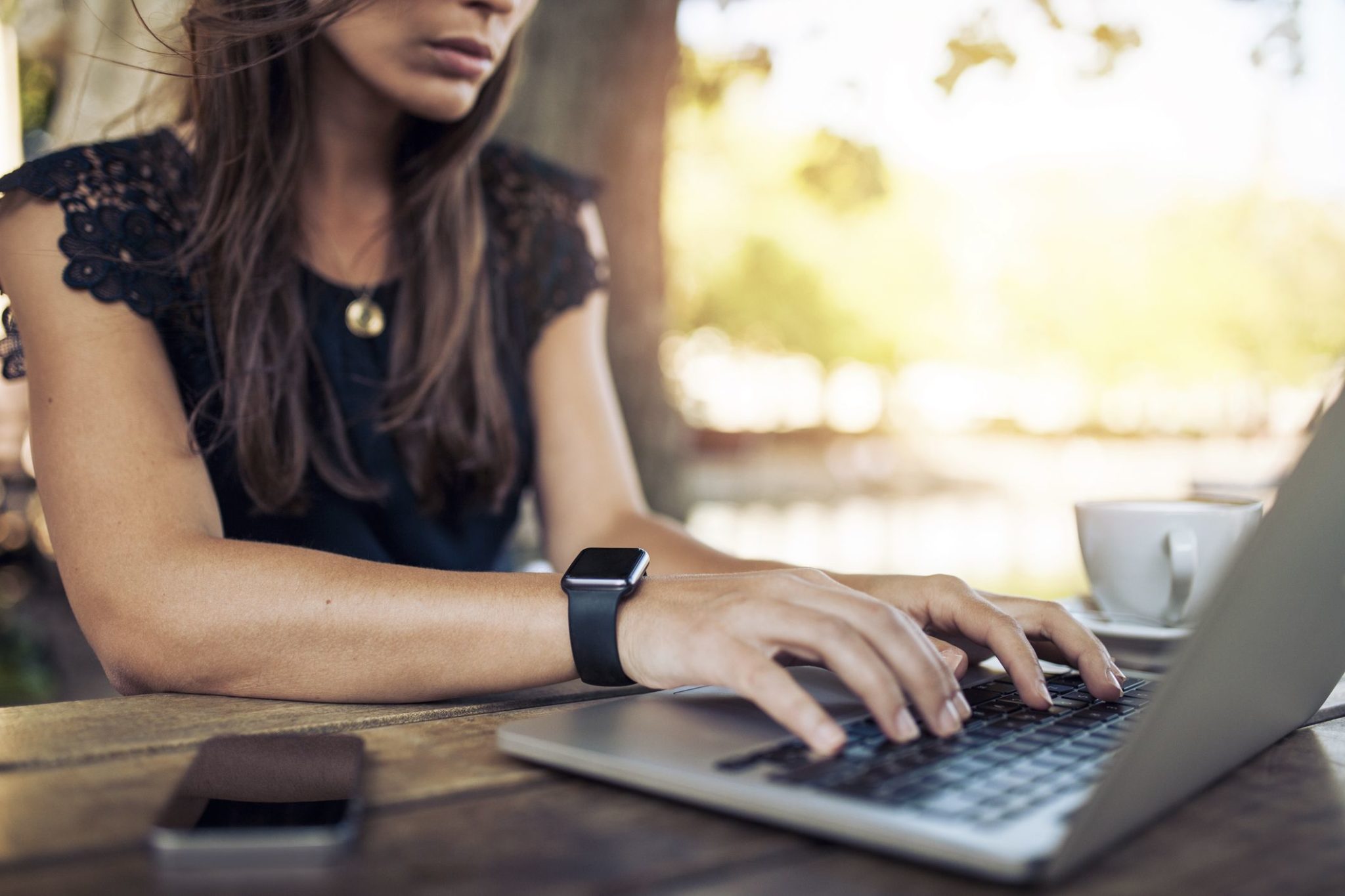 Young woman wearing smartwatch using laptop computer. Female working on laptop in an outdoor cafe.