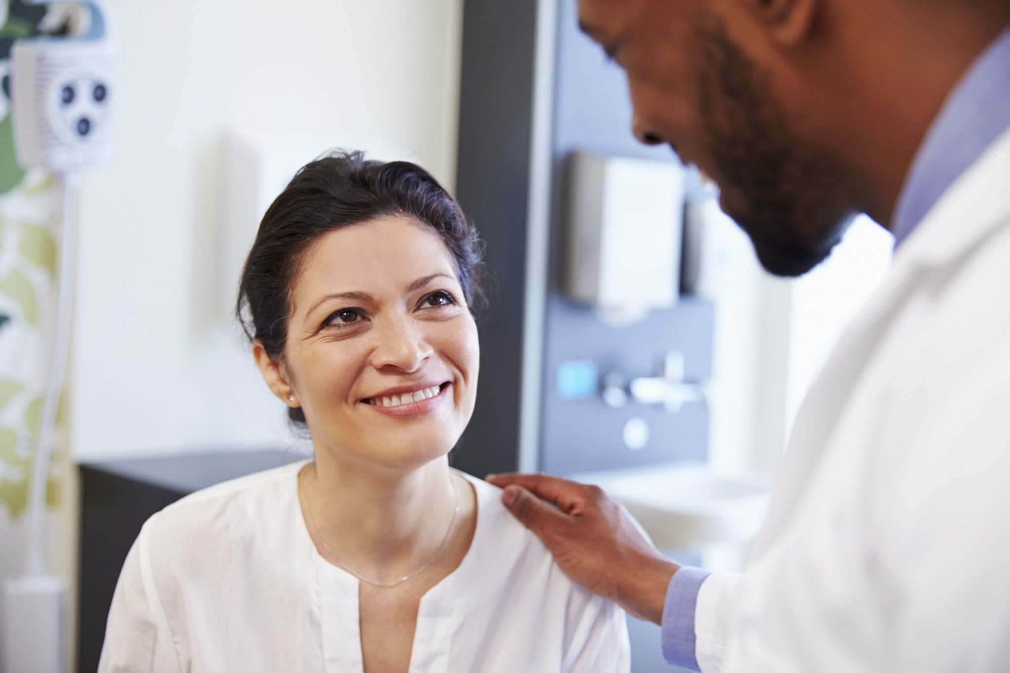 Female Patient Being Reassured By Doctor In Hospital Room