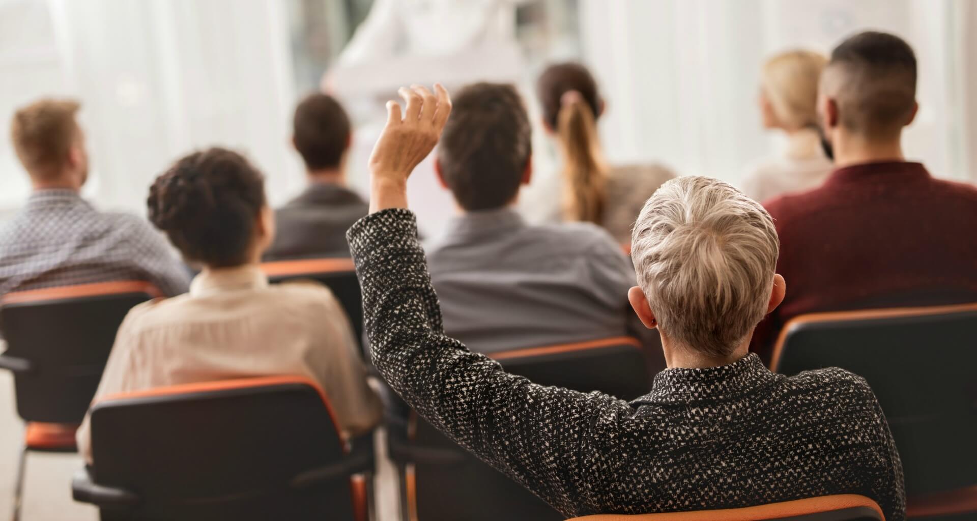 older woman raising her hand at a conference