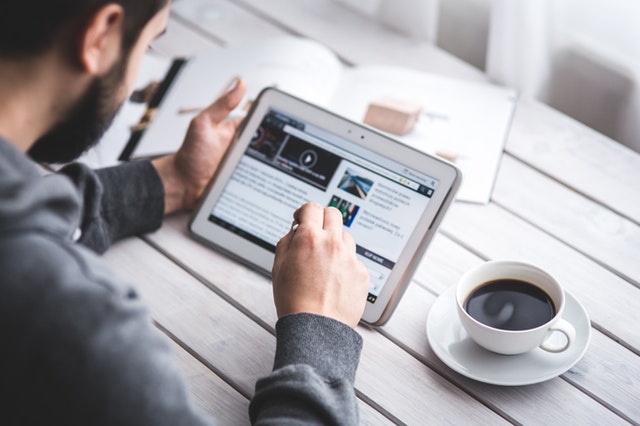 Man using a tablet while drinking a cup of coffee